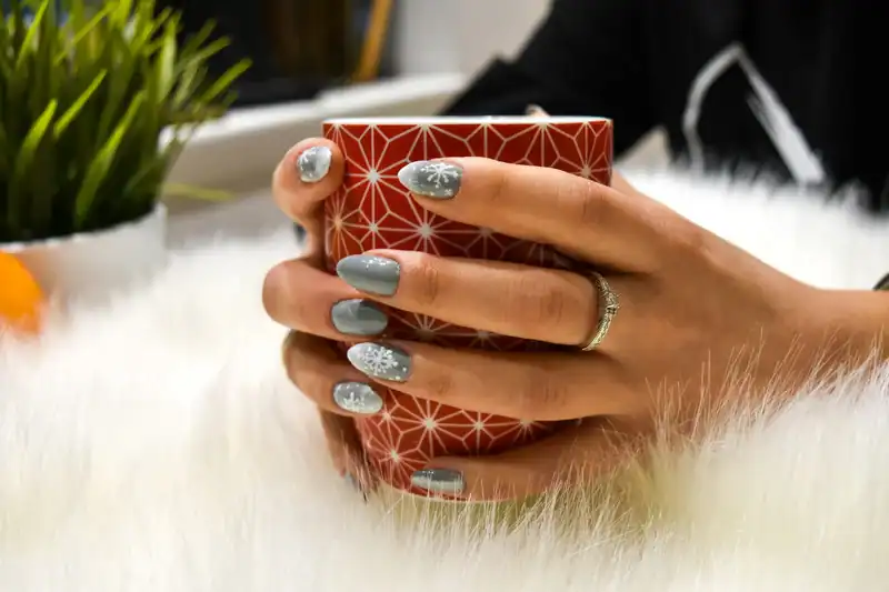 Elegant winter-themed gel nail design with snowflake accents on gray polish.