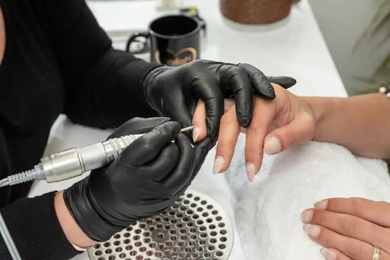 Nail technician performing custom nail design on a client's hand with electric pen tool.