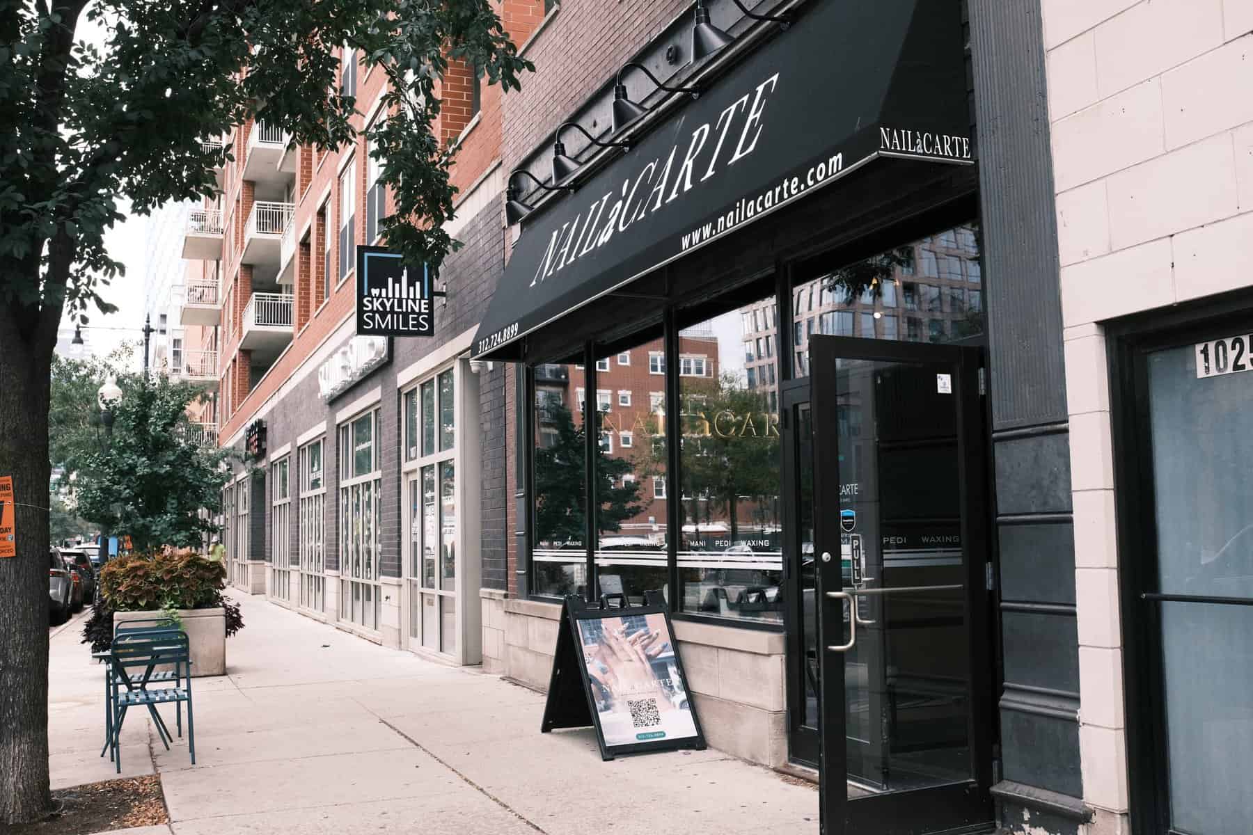 Chic nail salon storefront with black signage and large windows in an urban setting, specializing in manicure and pedicure services.