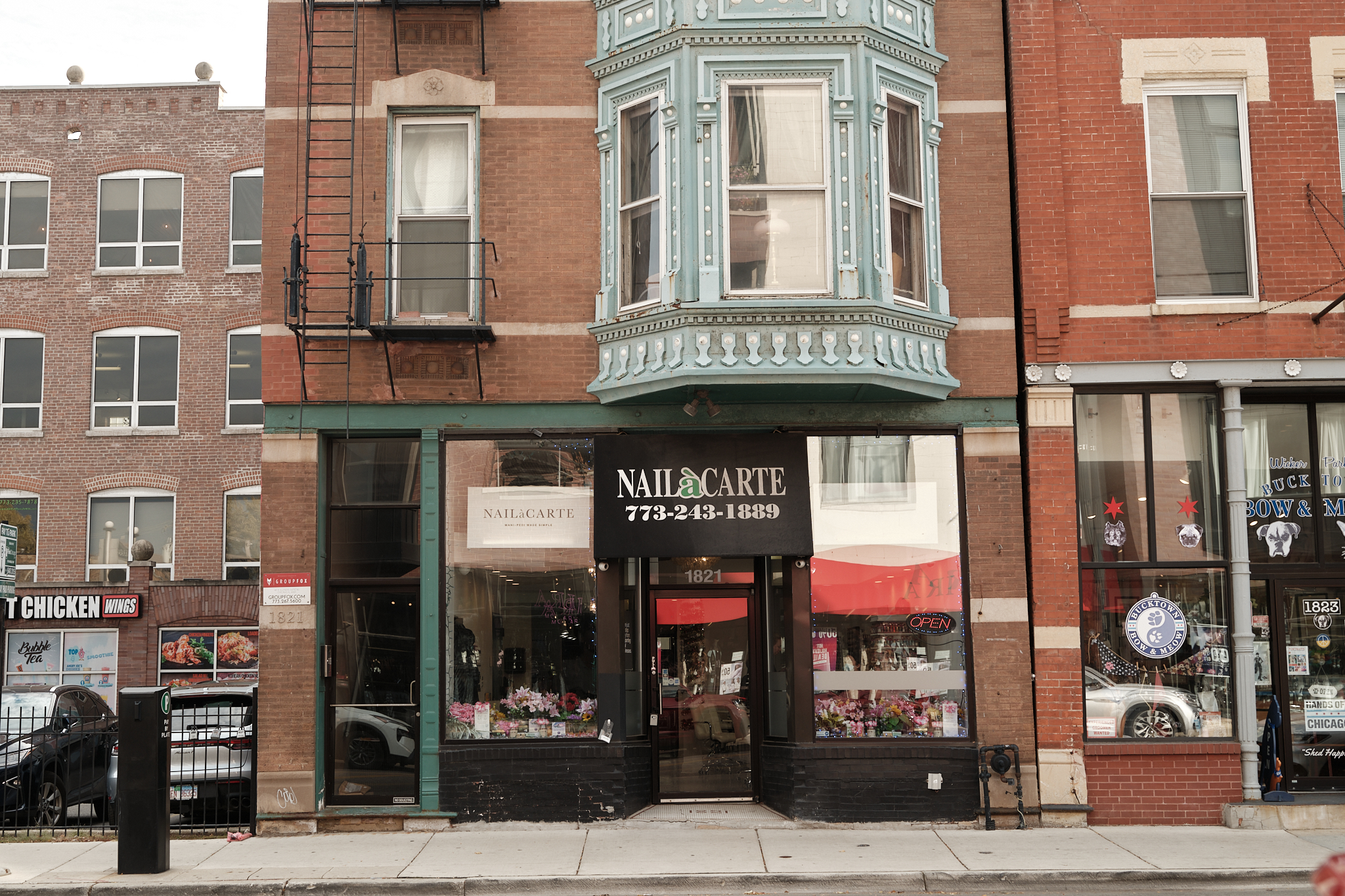 Elegant nail salon storefront with vintage-style building exterior, floral window displays, and modern signage, located in an urban shopping district.