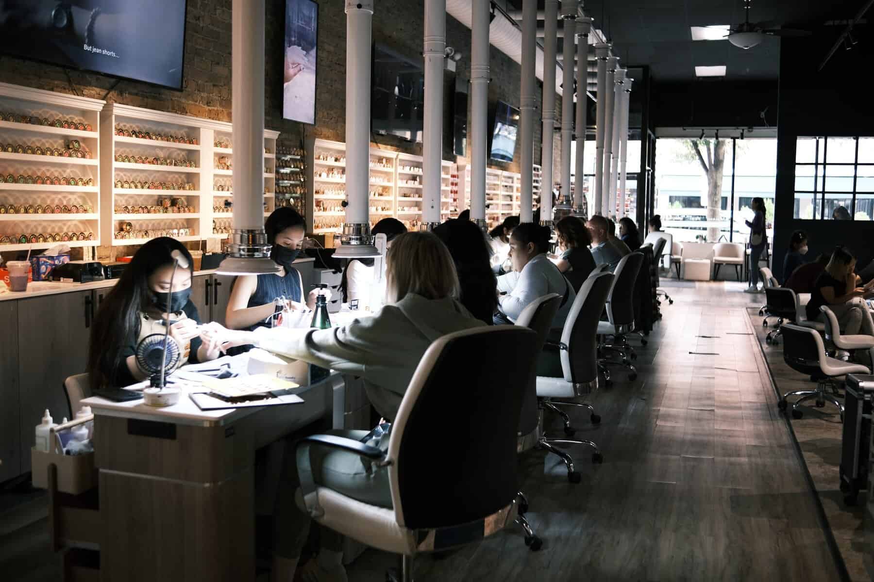 Bright nail salon with technicians performing manicures, modern decor, and a spacious, inviting atmosphere.