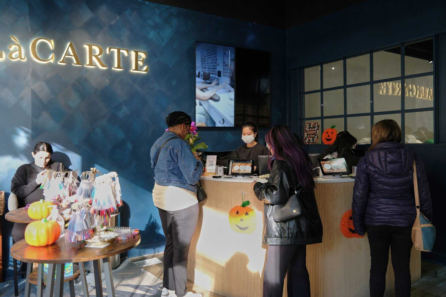 Bright nail salon reception at NAILàCARTE with customers and staff smiling; stylish, modern, and welcoming environment.