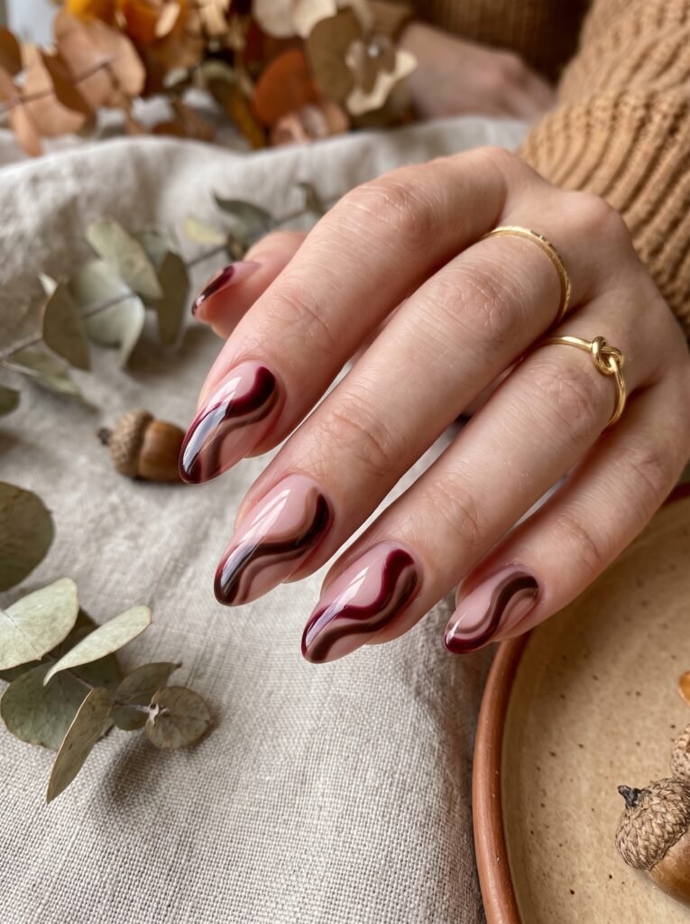 Rich oxblood burgundy and dark cacao fluid swirl lines on blush canvas for burgundy fall nails Gold Coast.